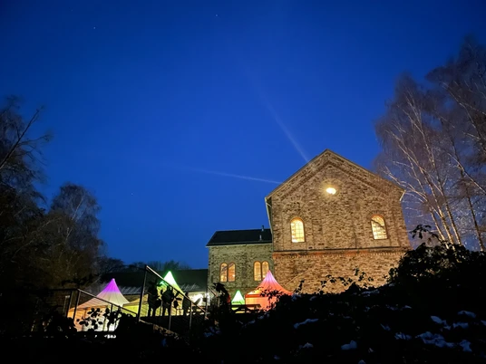 Piesberger Weihnachtzauber Abendstimmung.jpg Ein historisches Backsteingebäude beleuchtet den Nachthimmel; bunte Lichter im Vordergrund.A historic brick building illuminates the night sky; colorful lights in the foreground.En historisk murstensbygning lyser op på nattehimlen; farverige lys i forgrunden.Een historisch bakstenen gebouw verlicht de nachtelijke hemel; kleurrijke lichten op de voorgrond.