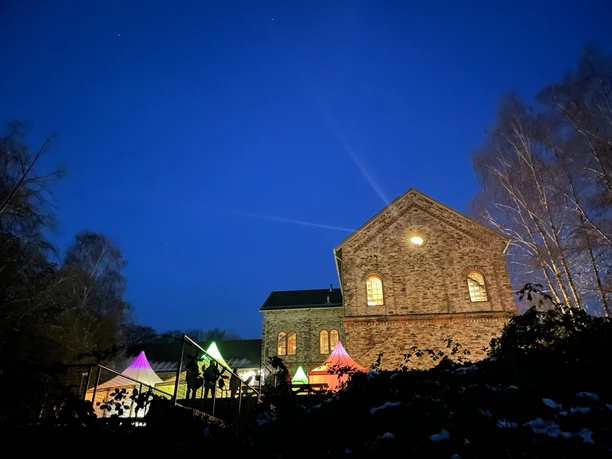 Ein historisches Backsteingebäude beleuchtet den Nachthimmel; bunte Lichter im Vordergrund.