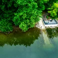 barrierefreie Badestelle an der Brucher Talsperre Luftaufnahme eines bewaldeten Seeufers mit kleinem Steg und Menschen beim Entspannen am Wasser.