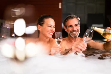 bad-driburg-graeflicher-park-health-resort-hotel-spa-28.jpg Ein Paar genießt gemeinsam ein Glas Sekt in einem sprudelnden Whirlpool, lächelnd und entspannt.