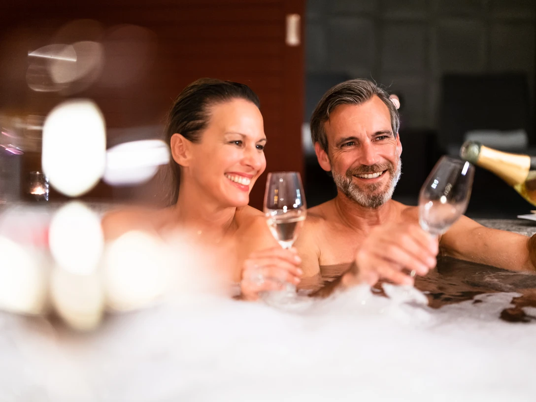 bad-driburg-graeflicher-park-health-resort-hotel-spa-28.jpg Ein Paar genießt gemeinsam ein Glas Sekt in einem sprudelnden Whirlpool, lächelnd und entspannt.