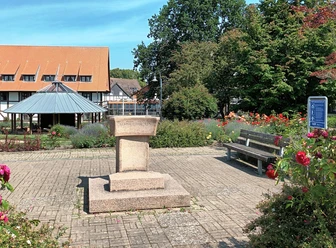 Steinernes Armtauchbecken auf einem gepflasterten Platz im Rosengarten vor einem Fachwerkhaus.