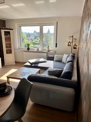 Wohnzimmer der Ferienwohnung im Weserbergland Lichtdurchflutetes Wohnzimmer mit Couch und hochwertigem Couchtisch aus Holz, Vitrine aus Holz und Glas.