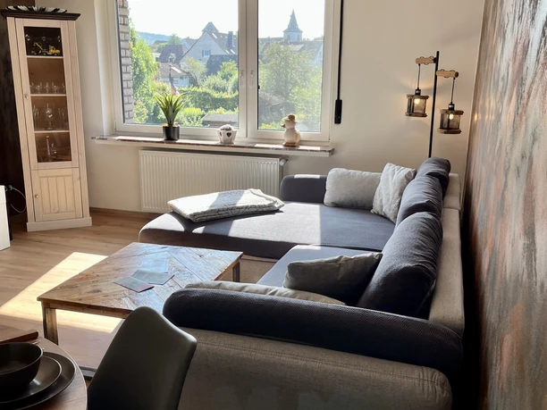 Wohnzimmer der Ferienwohnung im Weserbergland Lichtdurchflutetes Wohnzimmer mit Couch und hochwertigem Couchtisch aus Holz, Vitrine aus Holz und Glas.