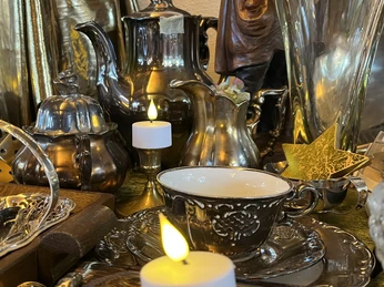 Silbernes Tischgeschirr, darunter Teekanne, Milchkännchen und Tasse, umgeben von Kerzenlicht.