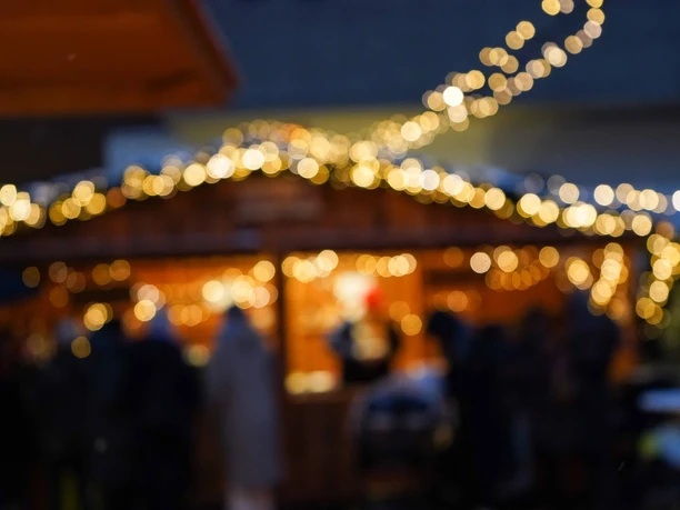 Sülzer Christmas Village Colorful lights in front of a blurred wooden house at a Christmas market at dusk.
