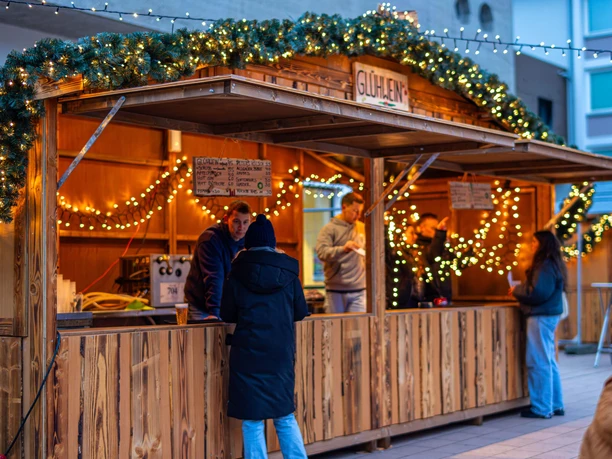 Sülzer Christmas Village An illuminated Christmas market stall with people and decorative lights.