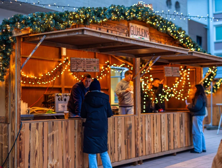 Sülzer Christmas Village Ein beleuchteter Weihnachtsmarktstand mit Personen und dekorativen Lichtern.An illuminated Christmas market stall with people and decorative lights.