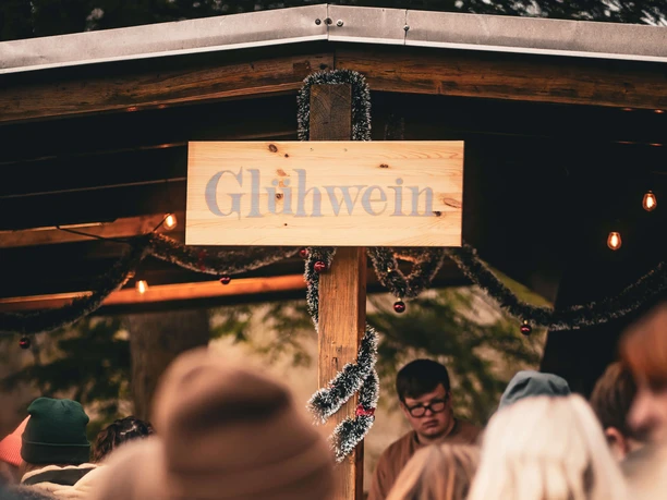 Veihnachtsmarkt-RosaRot-eV_1101.jpg Menschen vor einer Glühweinbude mit Deko und Lichtern auf einem Weihnachtsmarkt