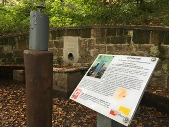 Rastplatz Riechen am Weg für Genießer - Urheber Stadt Werther.JPG Duftstation im Wald mit Infotafel und Zerstäuber, umrahmt von einer Steinmauer, herbstliche Blätter am Boden.