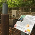 Rastplatz Riechen am Weg für Genießer - Urheber Stadt Werther.JPG Duftstation im Wald mit Infotafel und Zerstäuber, umrahmt von einer Steinmauer, herbstliche Blätter am Boden.