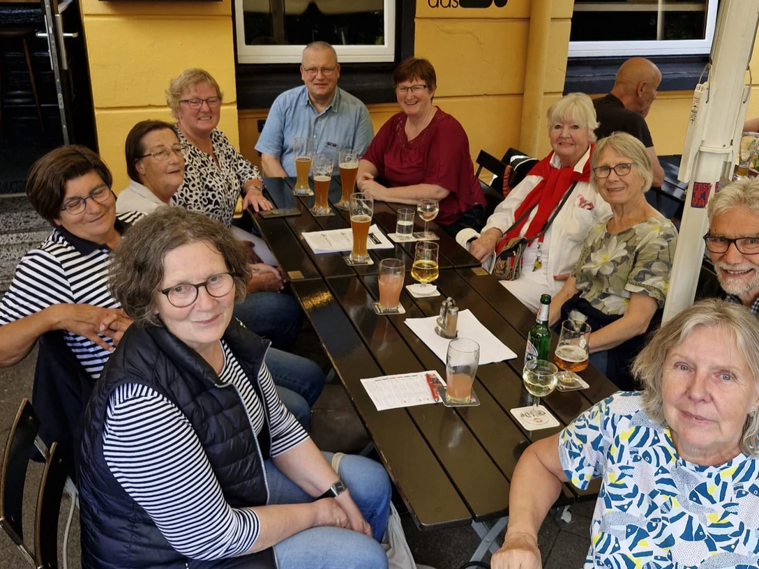 "Kontakt-Börse" Gruppe älterer Menschen in geselliger Runde an einem Tisch im Freien mit Getränken und guter Laune.