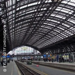 Gewölbtes Glasdach des Kölner Hauptbahnhofs mit geschäftigem Bahnsteig und wartenden Reisenden.
