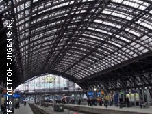 Gewölbtes Glasdach des Kölner Hauptbahnhofs mit geschäftigem Bahnsteig und wartenden Reisenden.