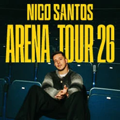Nico Santos sitzt in einem leeren Theater, umgeben von leeren, blauen Sitzreihen.