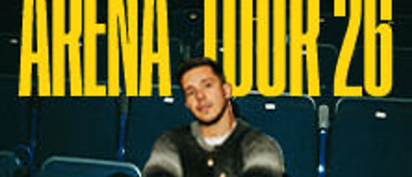 Nico Santos sitzt in einem leeren Theater, umgeben von leeren, blauen Sitzreihen.