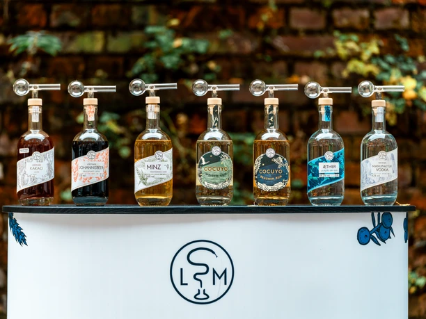 Produktvielfalt der Leipziger Spirituosen Manufaktur - Regionale Produkte aus Leipzig Aufgreit auf einem kleinen Tresen mit dem Logo der Leipziger Spirituosen Manufaktur stehen alle erhältlichen Produkte der Marke