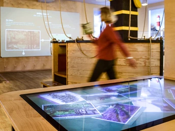 Menschenbewegung in interaktiver Museumsausstellung mit modernen digitalen Displays und Holzelementen.