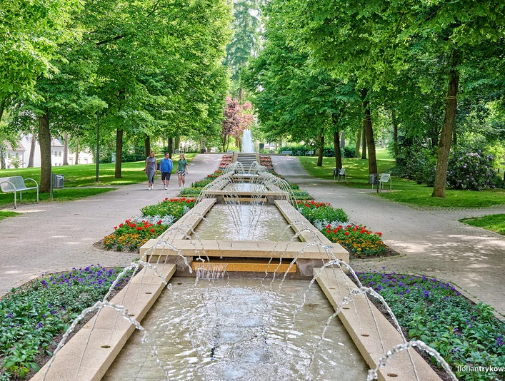 Brunnen im Kneipp-Kurpark Bad Camberg In der Mitte ist ein Kaskadenbrunnen zu sehen, links und rechts davon laufen jeweils zwei Personen.