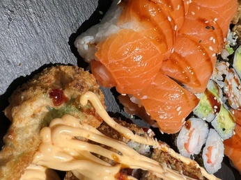 Frisch zubereitetes Sushi mit Lachs, Avocado und Sesam, kunstvoll auf einer Schieferplatte arrangiert.