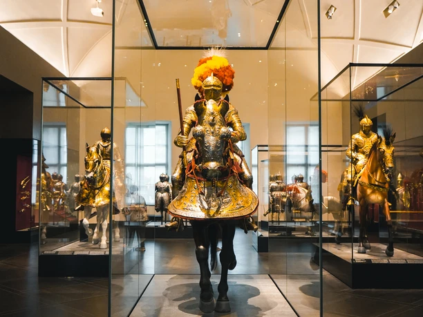 Einblicke in die Rüstkammer.jpg Ritterrüstung auf einem Pferd in einem modernen, gut beleuchteten Museumsausstellungsraum.