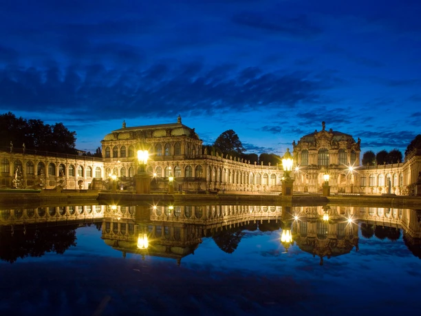 Zwinger Dresden.jpg Beleuchteter Zwinger in Dresden bei Nacht, mit Spiegelbild im Wasser.