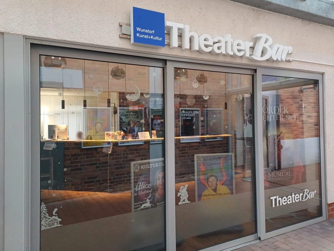 TheaterBar_Aussenansicht Eingang der TheaterBar in Wunstorf mit Glasfront, Plakaten und einem blauen Schild über der Tür.