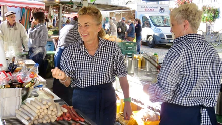Imbiss-Piske Eine lächelnde Frau steht an einem Marktstand am Grill.