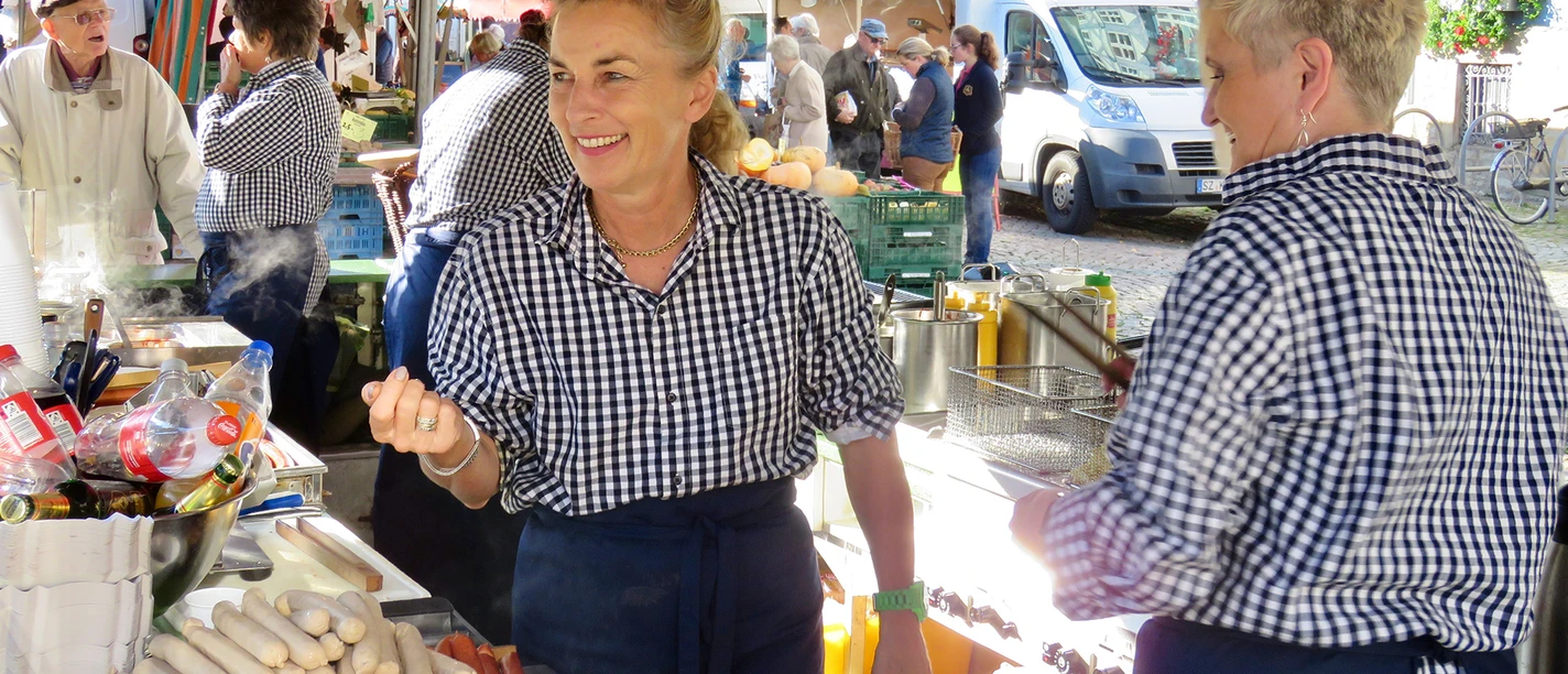 Imbiss-Piske Eine lächelnde Frau steht an einem Marktstand am Grill.
