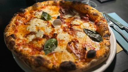 Pizza mit geschmolzenem Mozzarella und Basilikumblättern, serviert auf einem weißen Teller.