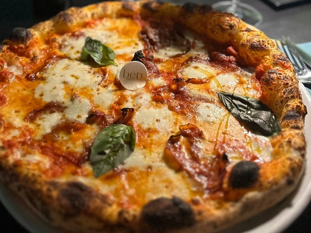 Pizza mit geschmolzenem Mozzarella und Basilikumblättern, serviert auf einem weißen Teller.