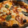 Pizza_Mozzarella_CCBYSA_Teutoburger Wald_Stadt_Schloß Holte-Stukenbrock.jpg Pizza mit geschmolzenem Mozzarella und Basilikumblättern, serviert auf einem weißen Teller.