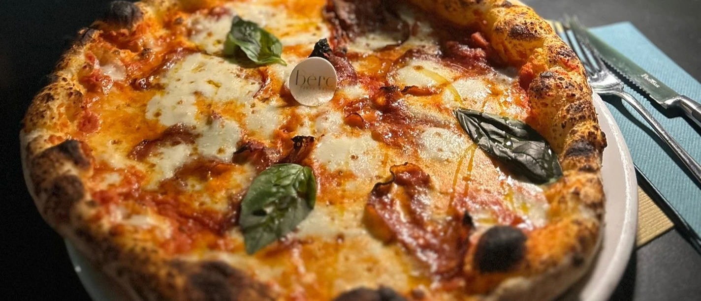 Pizza_Mozzarella_CCBYSA_Teutoburger Wald_Stadt_Schloß Holte-Stukenbrock.jpg Pizza mit geschmolzenem Mozzarella und Basilikumblättern, serviert auf einem weißen Teller.