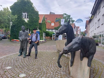 haller_willem.jpg Zwei Bronzeskulpturen in einer gepflasterten Straße zeigen Pferde und Männer bei einer Plauderei.