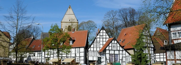haller_herz1.jpg Historische Fachwerkhäuser mit roten Dächern und einem Kirchturm im Hintergrund unter klarem Himmel.