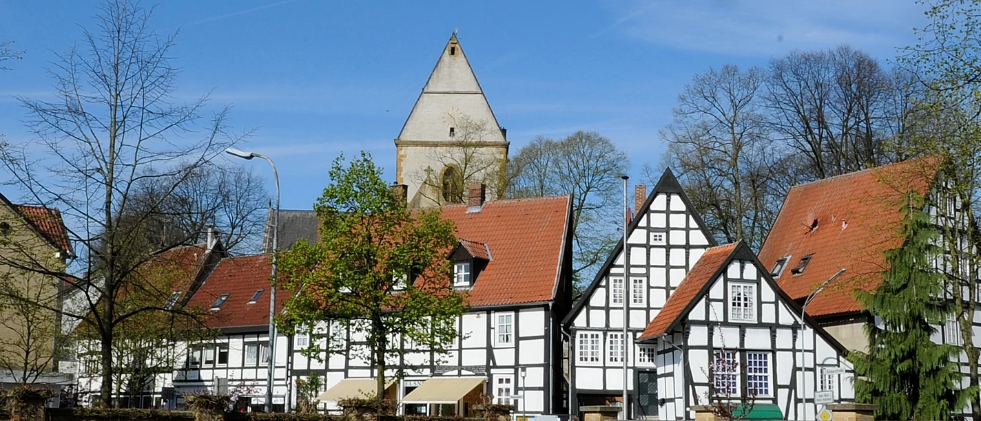 haller_herz1.jpg Historische Fachwerkhäuser mit roten Dächern und einem Kirchturm im Hintergrund unter klarem Himmel.