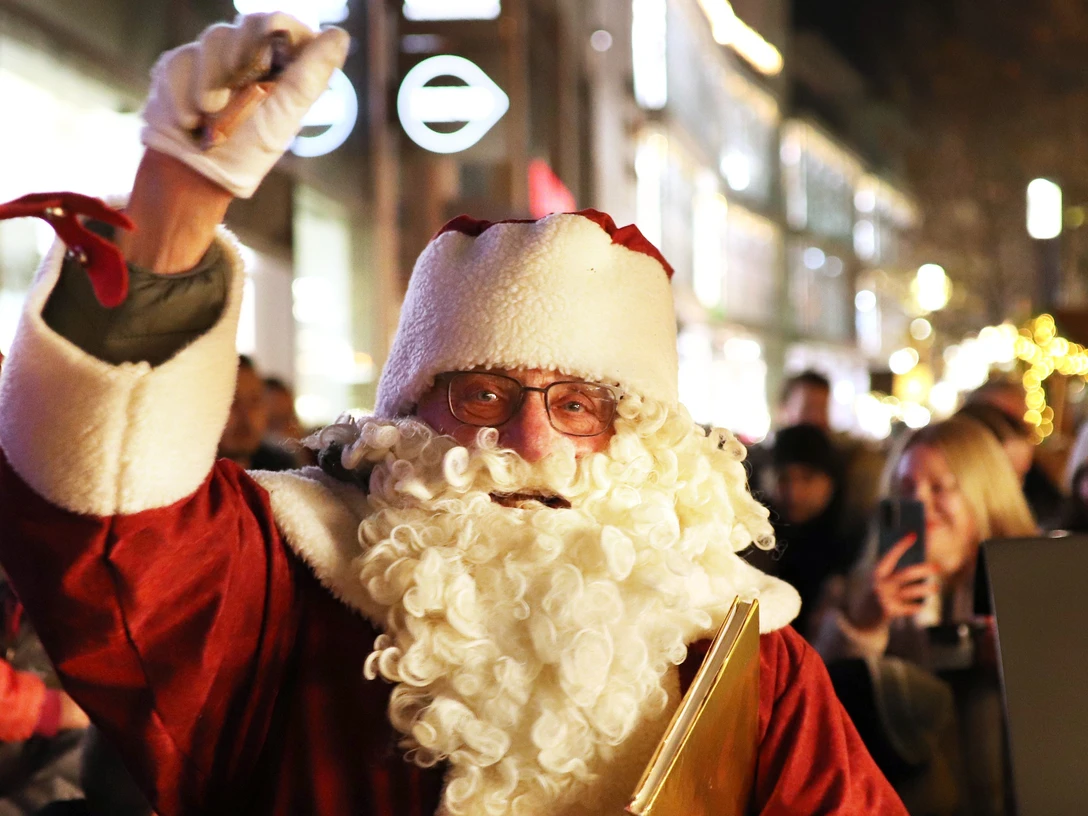 Nikolaus.JPG Nikolaus in rotem Mantel mit weißem Bart winkt in stimmungsvoll beleuchteter Einkaufsstraße.