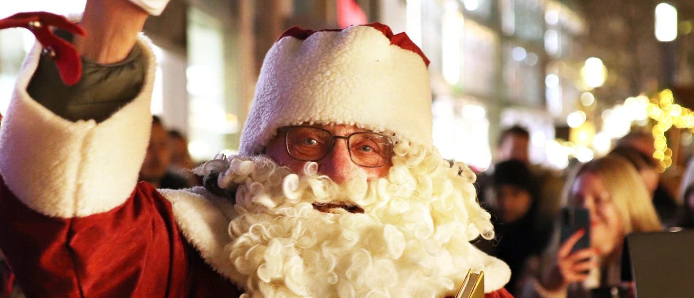 Nikolaus.JPG Nikolaus in rotem Mantel mit weißem Bart winkt in stimmungsvoll beleuchteter Einkaufsstraße.