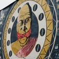 Mural Ein großflächiges Wandgemälde zeigt einen älteren Mann mit Brille, dessen Mund von einem roten Tuch bedeckt ist, eingerahmt in einem stilisierten Musterkreis.A large mural shows an elderly man with glasses, his mouth covered by a red cloth, framed in a stylized patterned circle.