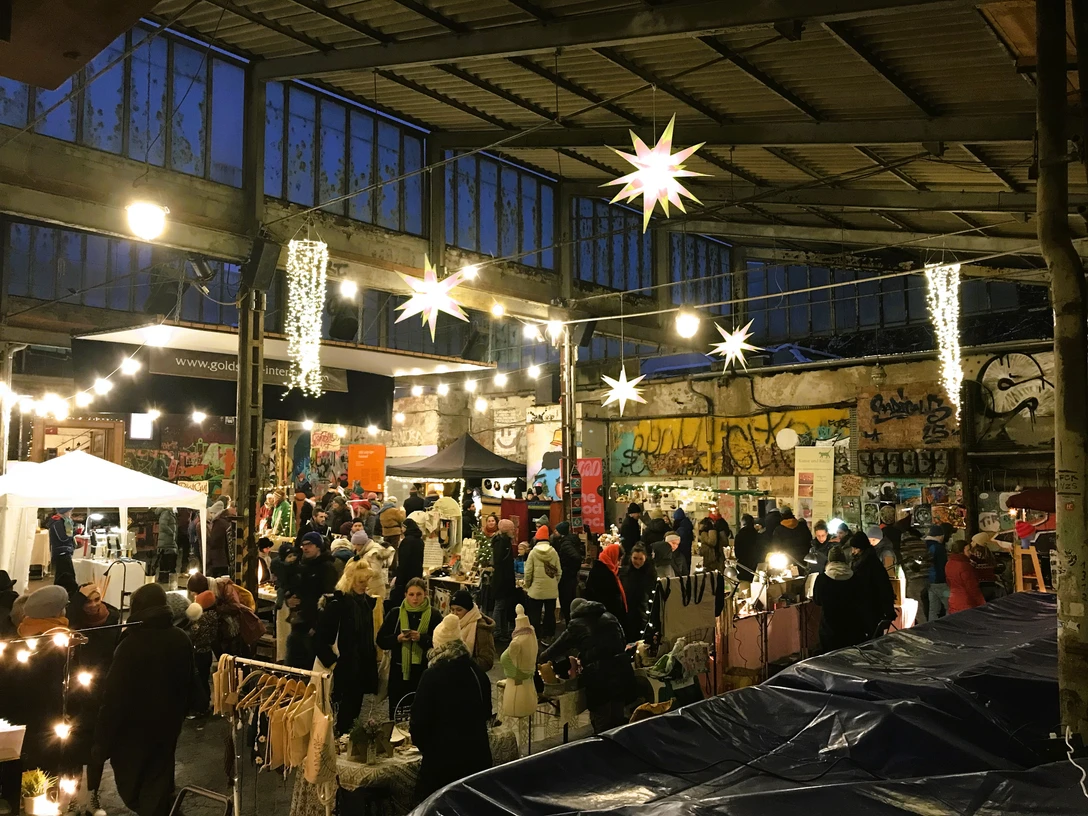 Weihnachtsmarkt auf der Feinkost - Weihnachten in Leipzig Auf dem hell erleuchteten Gelände der Feinkost stöbern Besucherinnen und Besucher am Abend an den zahlreichen Verkaufsständen