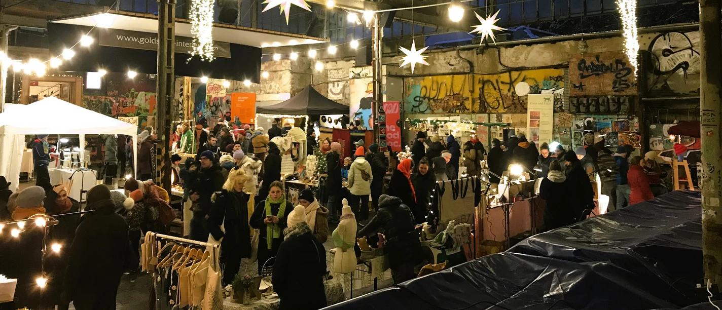 Weihnachtsmarkt auf der Feinkost - Weihnachten in Leipzig Auf dem hell erleuchteten Gelände der Feinkost stöbern Besucherinnen und Besucher am Abend an den zahlreichen Verkaufsständen