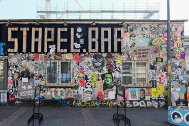Mural Eine bunte Street-Art-Wand zeigt Graffiti und Sticker in lebhaften Farben, flankiert von Baugerüsten.