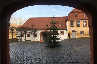 Blick durch einen Torbogen auf einen gepflasterten Innenhof mit einem Weihnachtsbaum und historischen Gebäuden.