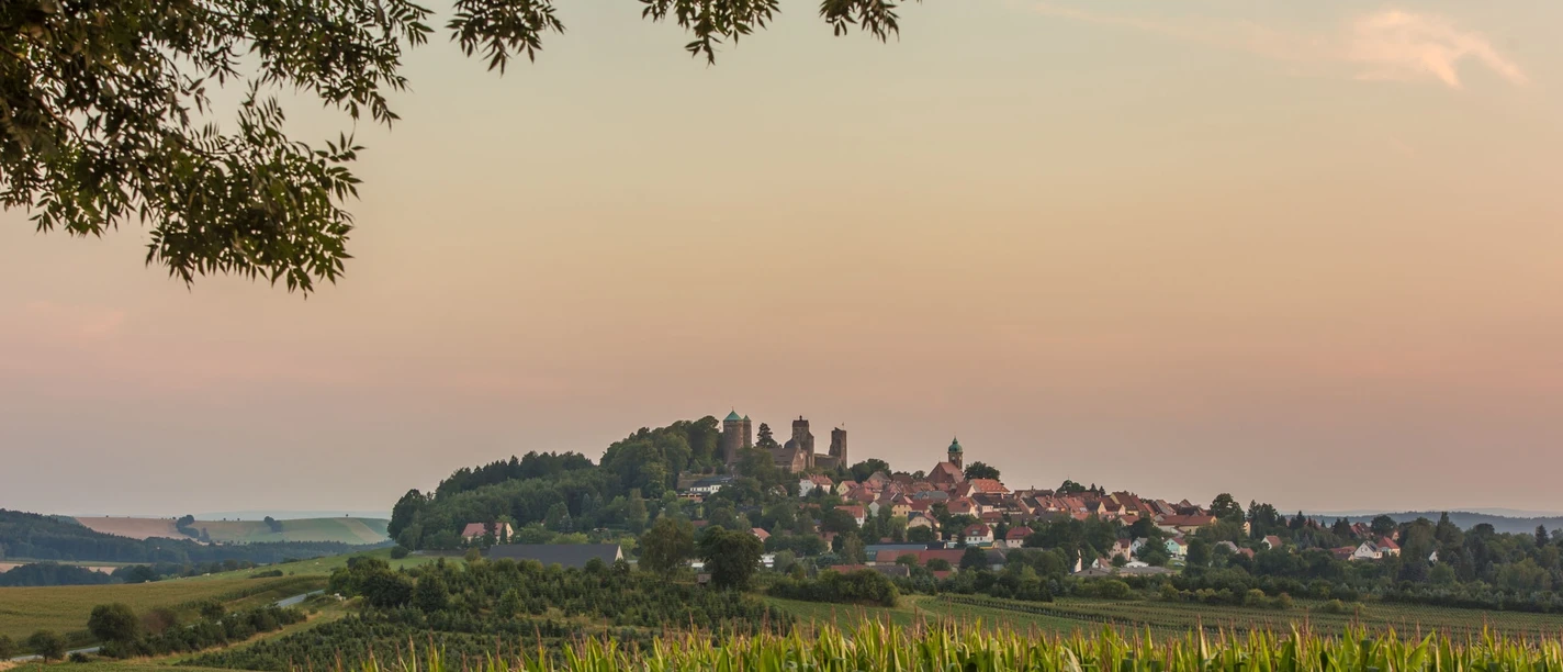 Burg Stolpen Blick auf Stolpen mit Burg Stolpen, umgeben von Feldern und Bäumen bei Sonnenuntergang.