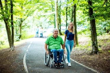 barrierefreier Weg an der Brucher Talsperre Senior im Rollstuhl auf Waldweg, begleitet von junger Frau; beide lächeln in grüner Umgebung.