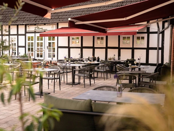 (C) La Fucina 2.jpg Gemütlicher Innenhof eines Restaurants mit Fachwerk, roten Sonnensegeln und stilvollen Sitzgelegenheiten.