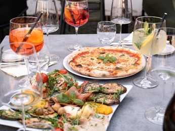 (C) La Fucina 3.jpg Italienische Speisen und Aperitifs auf einem gedeckten Tisch, einschließlich Pizza und Antipasti.