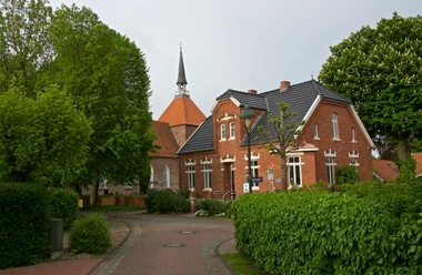 Warfendorf Rysum Backsteinhäuser und Kirche mit Spitzdach umgeben von Bäumen im historischen Warfendorf Rysum.