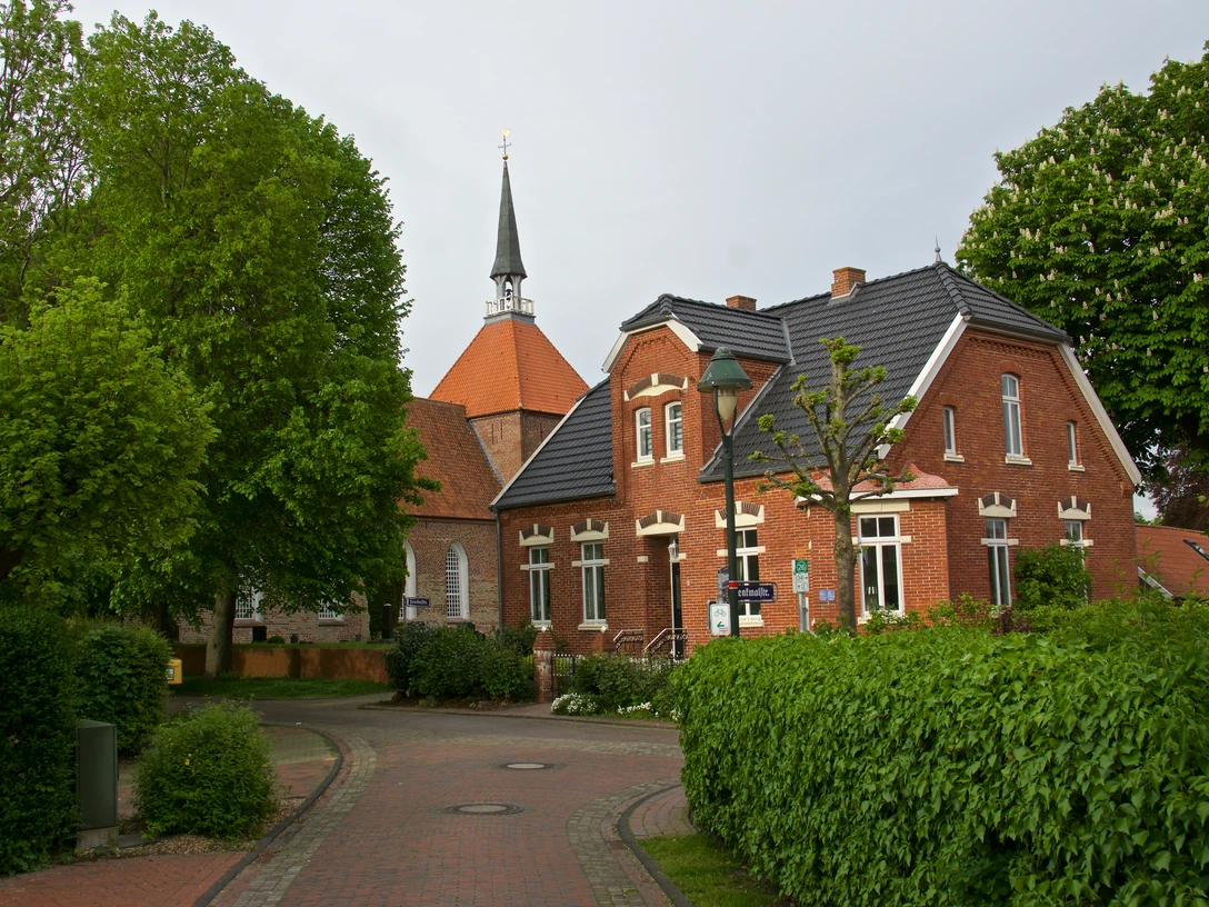 Warfendorf Rysum Backsteinhäuser und Kirche mit Spitzdach umgeben von Bäumen im historischen Warfendorf Rysum.
