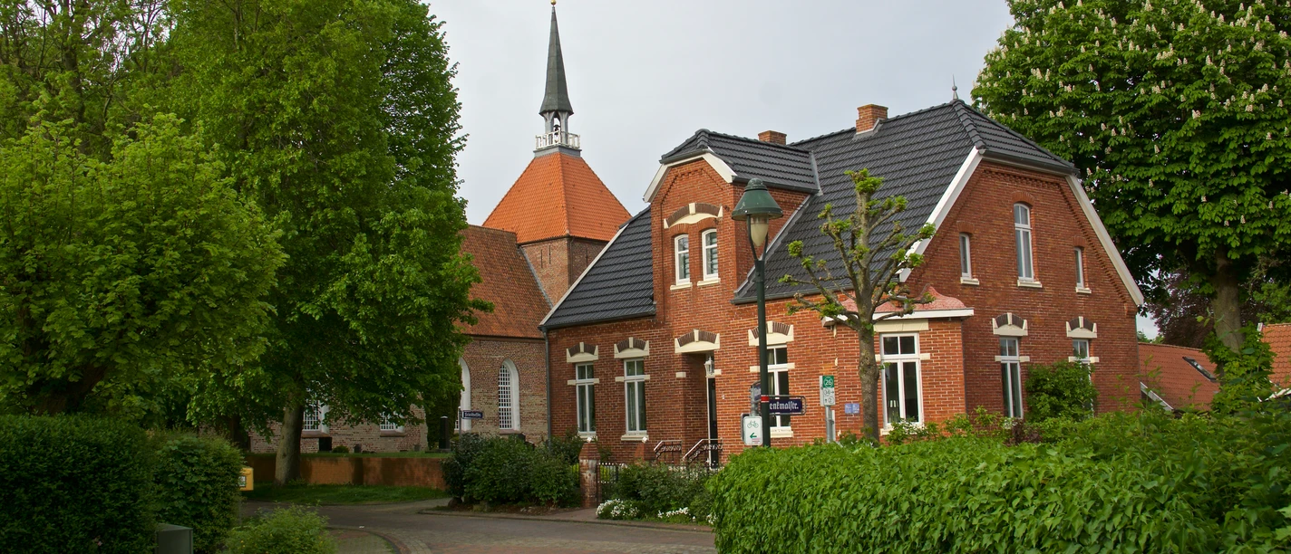 Warfendorf Rysum Backsteinhäuser und Kirche mit Spitzdach umgeben von Bäumen im historischen Warfendorf Rysum.